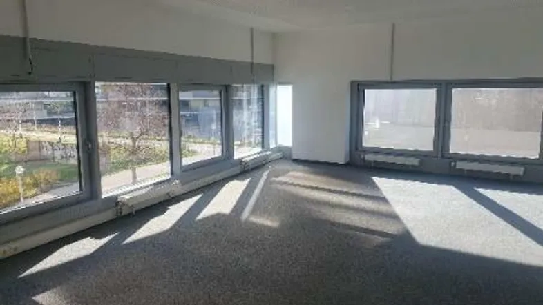 Heller Büroraum mit großen Fenstern, die viel Tageslicht hereinlassen und einen Blick nach draußen bieten.