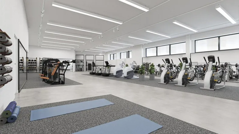 Großer, moderner Fitnessraum mit verschiedenen Trainingsgeräten, hellen Lichtverhältnissen und Yoga-Bereich.