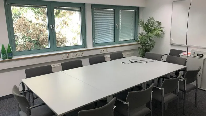 Heller Konferenzraum mit großem Tisch, bequemen Stühlen und Blick ins Grüne durch die Fenster.