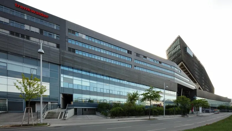 Moderne Bürogebäude-Fassade mit großen Glasflächen und dunklen Paneelen an einem hellen Tag.