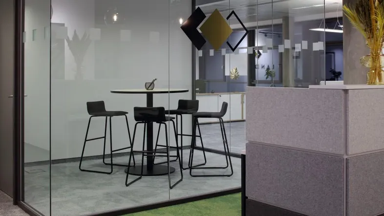 Moderner Bürobereich mit gläsernem Besprechungsraum, Stehtisch und Barhockern auf Teppichboden.