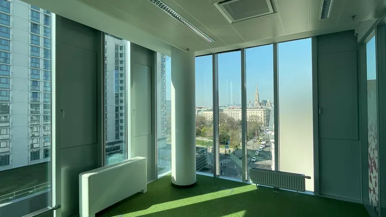 Helles Büro mit großen Fenstern, grünem Teppichboden und weitem Blick über die Stadt.
