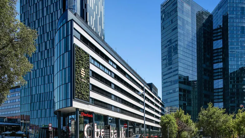 Modernes Bürogebäude mit Glasfassade und vertikaler Begrünung an der Straßenecke unter blauem Himmel.