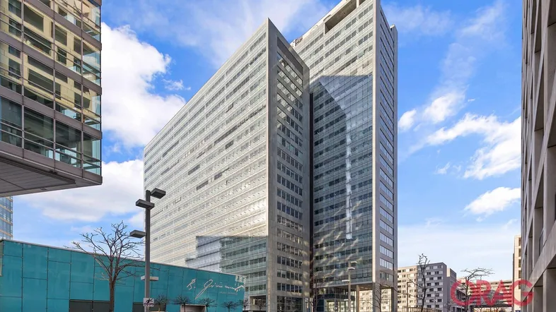Modernes Hochhaus mit markanter Glasfassade und klarem Himmel, umgeben von weiteren Gebäuden.