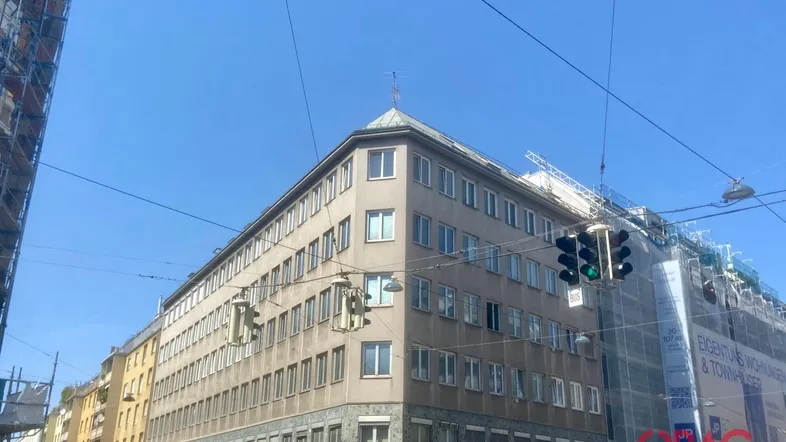 Gebäude an einer Straßenecke mit vielen Fenstern und Gerüsten an angrenzenden Gebäuden unter blauem Himmel.