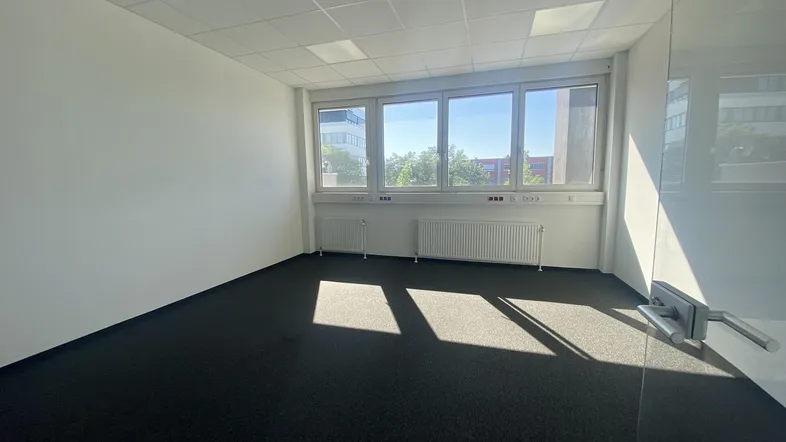 Helles und geräumiges Büro mit großen Fenstern, Teppichboden und viel Tageslicht.