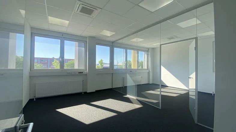 Helles und modernes Büro mit großen Fenstern, Teppichboden und Glaswänden, ideal für gewerbliche Nutzung.