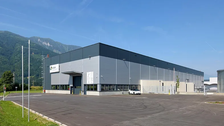 Modernes Industriegebäude mit grauer Fassade und weitem Blick auf die umliegende Berglandschaft unter blauem Himmel.