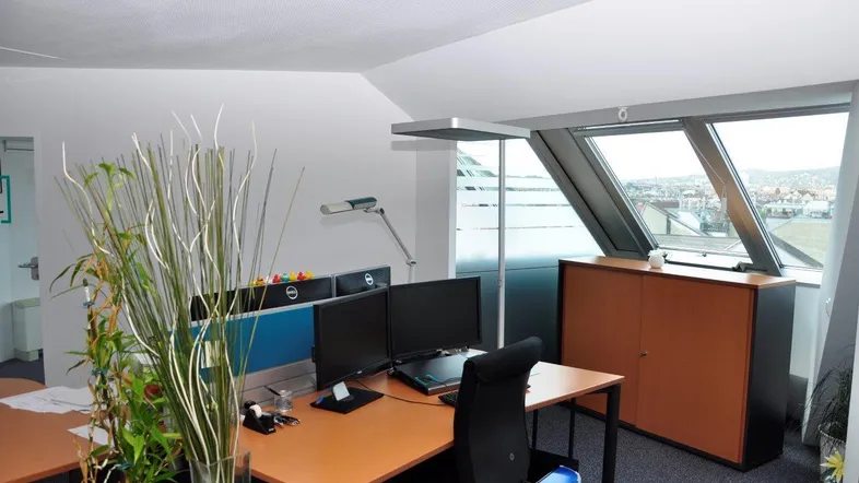Modernes Büro mit Dachschrägenfenstern und Blick über die Stadt, ausgestattet mit mehreren Arbeitsplätzen.