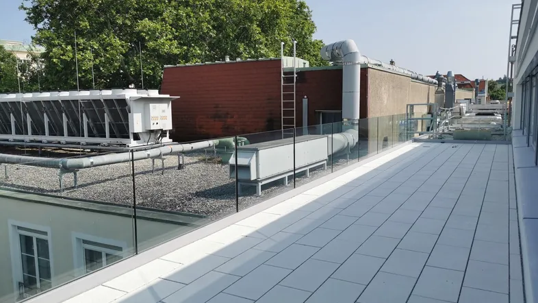 Geräumige Dachterrasse mit modernen weißen Fliesen, Glasgeländer und Blick auf die Umgebung.