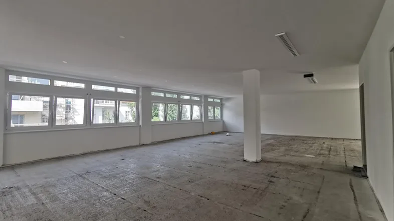 Großer, heller Büroraum mit vielen Fenstern und Rohbetonboden, bereit für den Ausbau.