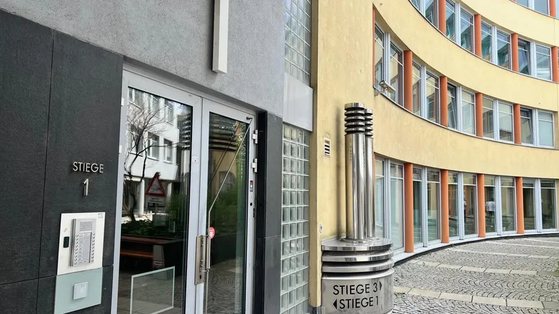 Eingangsbereich eines modernen Gebäudes mit Hausnummer 1 und Hinweisschildern zu den Stiegen.
