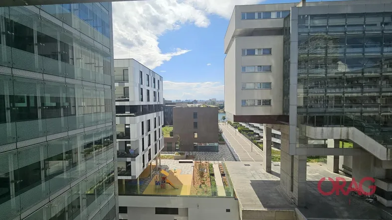 Blick aus einem Fenster auf moderne Gebäude, einen Spielplatz und den Himmel mit Wolken.