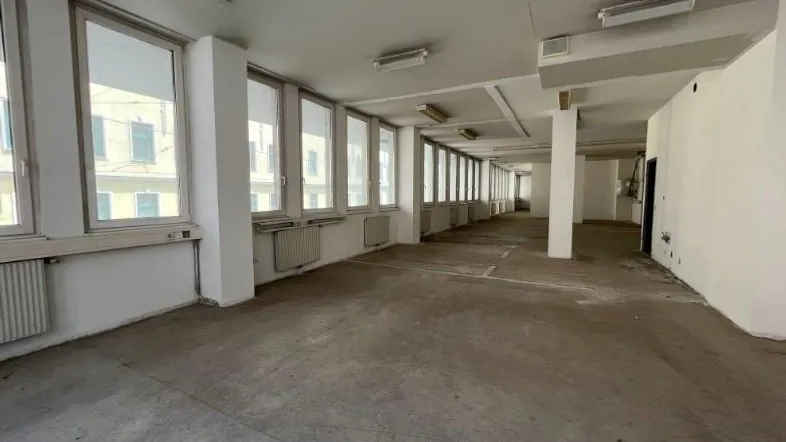 Großer, leerer Raum mit vielen Fenstern und Betonboden, ideal für Büro- oder Gewerbenutzung.