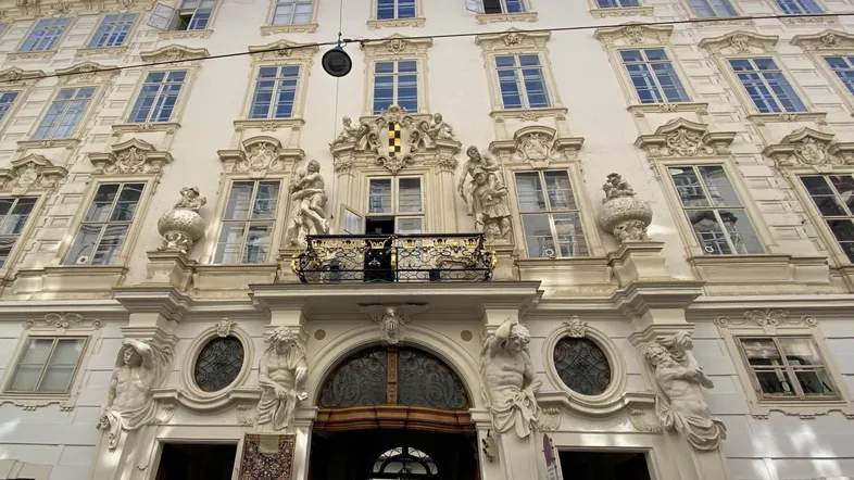 Prächtige historische Fassade eines Altbaus mit reich verzierten Fenstern, Skulpturen und einem kleinen Balkon.