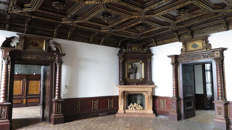 Prunkvoller Saal mit dunkler Holzvertäfelung, Kassettendecke und einem verzierten Kamin mit Spiegel.