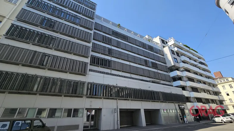 Modernes Bürogebäude mit vielen Fenstern und Jalousien an einer städtischen Straße.