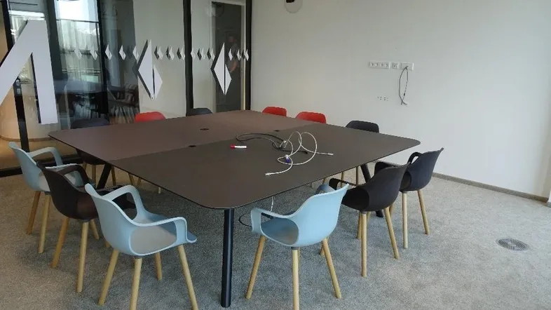 Moderner Konferenzraum mit großem Tisch und verschiedenen Stühlen, ideal für Besprechungen und Teamarbeit.