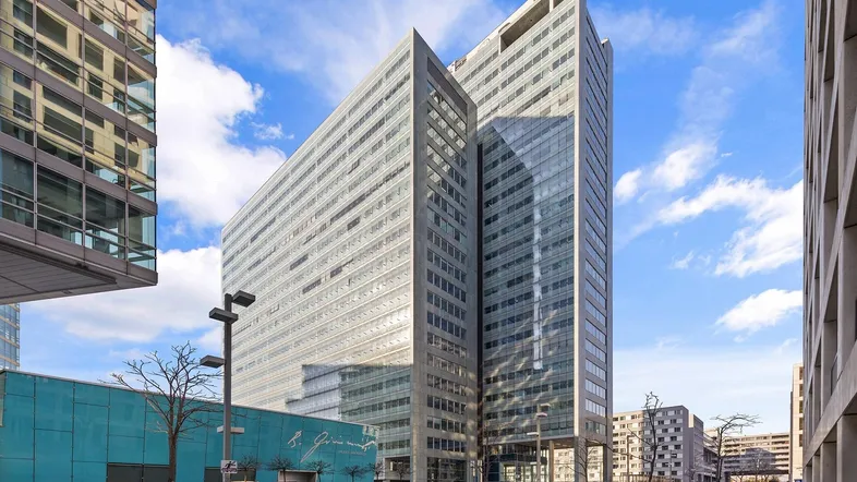 Modernes Hochhaus mit Glasfassade und klaren Linien unter blauem Himmel in urbaner Umgebung.