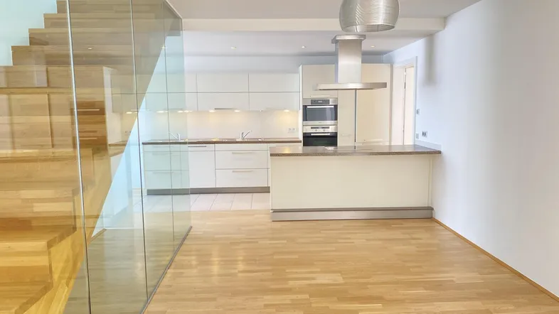 Moderner offener Wohn- und Essbereich mit integrierter Küche, Holztreppe und Glasgeländer.