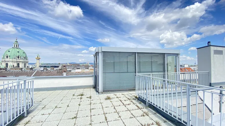 Geräumige Dachterrasse mit Fliesenboden und weitem Blick über die Stadt unter blauem Himmel.