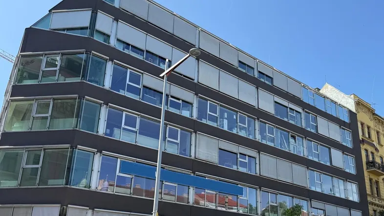 Modernes Bürogebäude mit großen Glasflächen und Jalousien unter blauem Himmel.