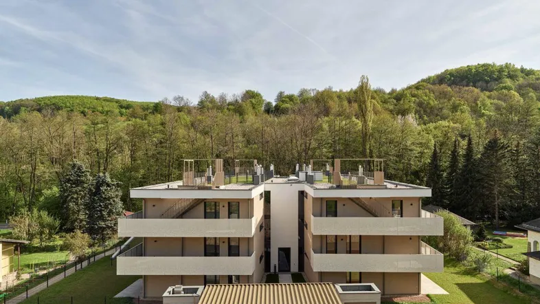 Modernes Mehrfamilienhaus mit mehreren Balkonen und Terrassen, eingebettet in eine grüne Hügellandschaft.