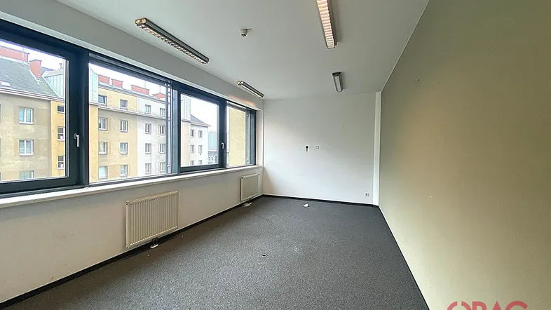 Geräumiges Büro mit Teppichboden und großen Fenstern, die viel Tageslicht hereinlassen und einen Blick auf die Stadt bieten.