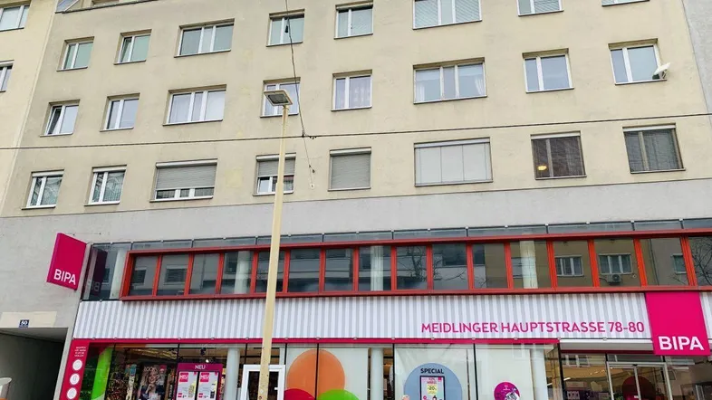 Gebäude mit mehreren Stockwerken und einer Ladenfront im Erdgeschoss an einer belebten Straße.