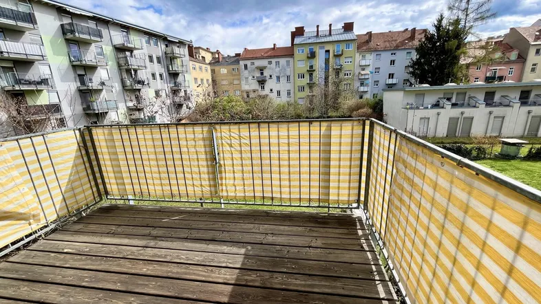 Balkon mit Holzboden und gestreiftem Sichtschutz bietet Blick auf den Innenhof und umliegende Gebäude.