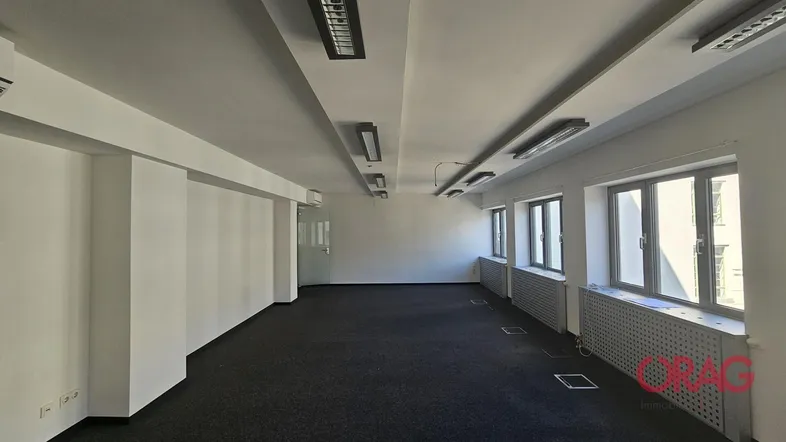 Geräumiges, leeres Büro mit Teppichboden, großen Fenstern und Deckenbeleuchtung, bereit zur individuellen Gestaltung.
