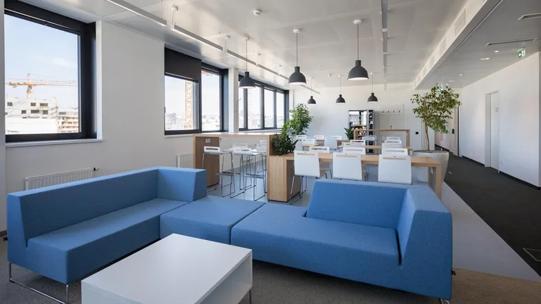Moderner Loungebereich mit bequemen blauen Sofas, weißen Tischen und Blick auf eine Baustelle.