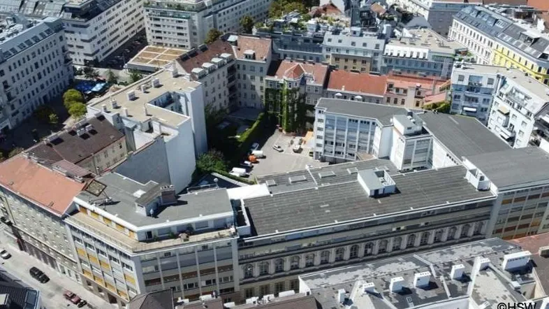 Luftaufnahme eines dicht bebauten Stadtblocks mit verschiedenen Gebäuden, Flachdächern und einem Innenhof mit Parkplätzen.