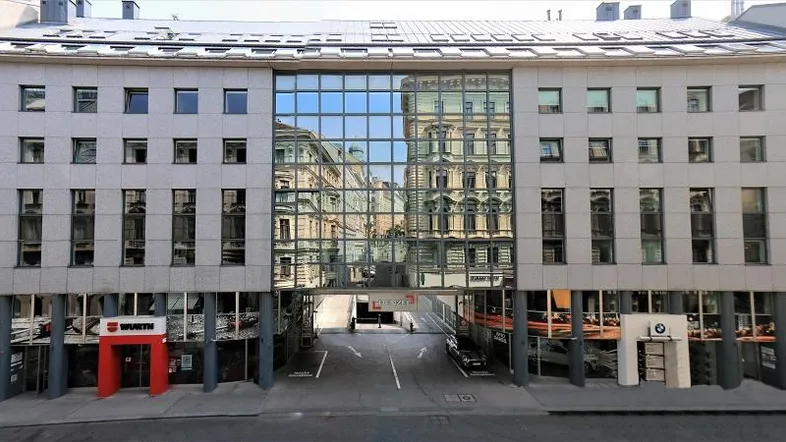 Modernes Geschäftsgebäude mit großer Glasfassade, die die umliegende Architektur widerspiegelt.