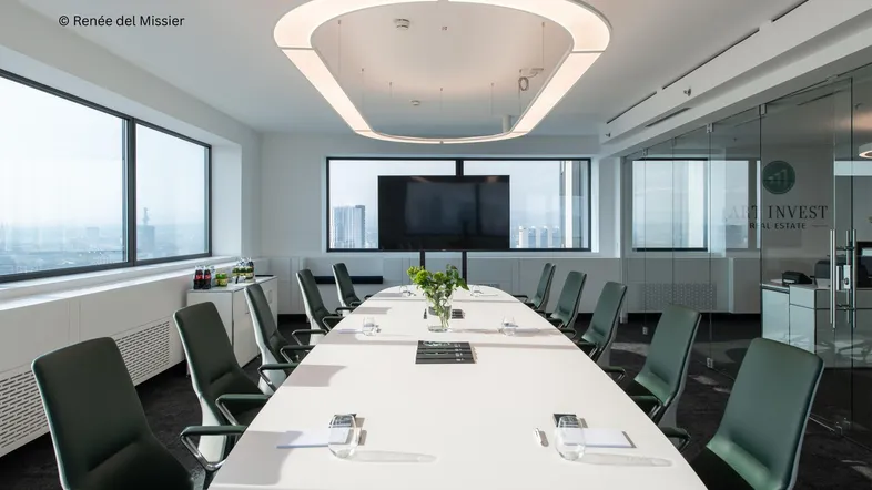 Moderner Konferenzraum mit langem weißen Tisch, ergonomischen Stühlen und großen Fenstern mit Stadtblick.