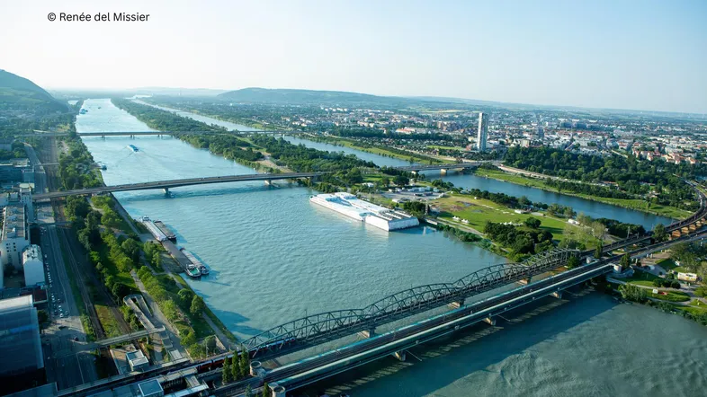 Luftaufnahme einer Stadt mit mehreren Flüssen, Brücken und grünen Ufern unter klarem Himmel.