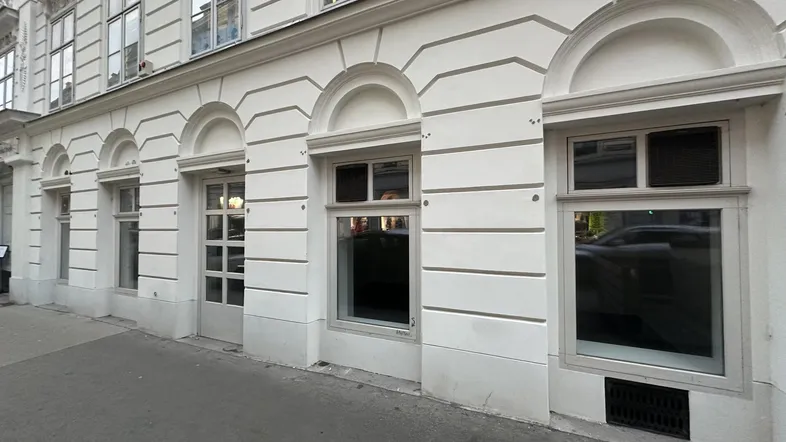Die Fassade eines klassischen Altbaus mit großen Fenstern und einem einladenden Eingangsbereich zur Straße.