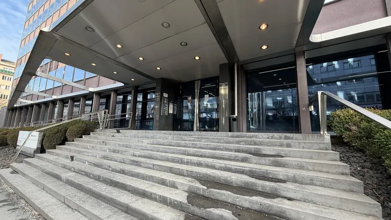 Eingangsbereich eines modernen Bürogebäudes mit breiter Steintreppe und überdachtem Zugang.