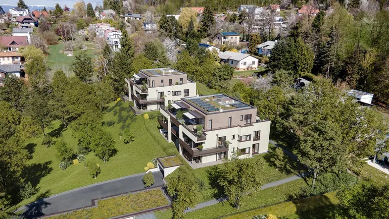 Luftaufnahme von zwei modernen Wohngebäuden mit Flachdächern und Photovoltaikanlagen auf einem grünen Hügel.