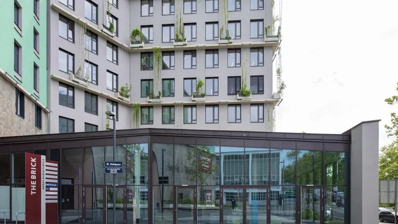 Modernes Gebäude mit großer Glasfassade im Erdgeschoss und begrünten Balkonen in den oberen Etagen.