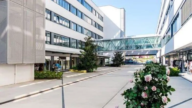 Moderne Bürogebäude mit Glasfassaden und einer verbindenden Fußgängerbrücke, umgeben von gepflegten Außenanlagen und Wegen.