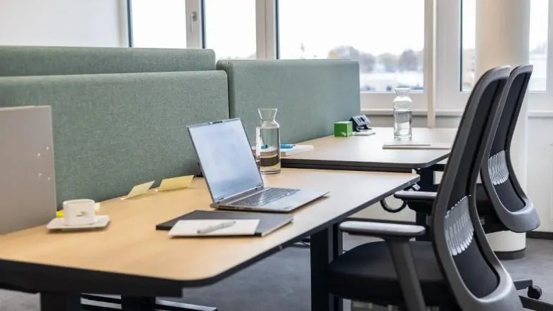 Moderner Büroraum mit ergonomischen Stühlen, Laptops auf Schreibtischen und Blick nach draußen.