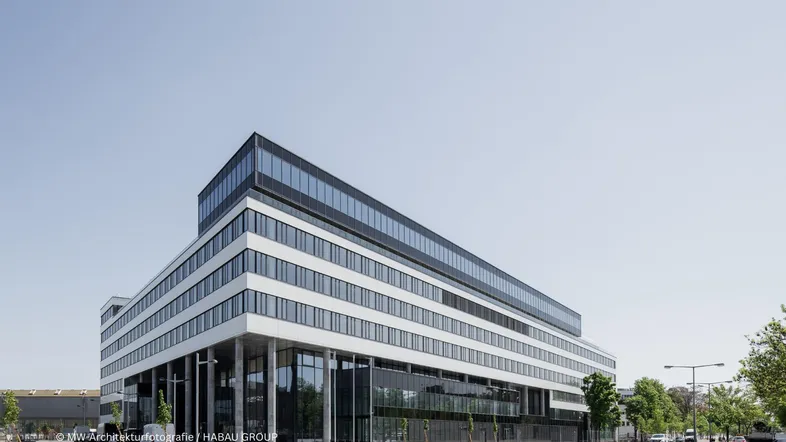 Modernes Bürogebäude mit weißer Fassade, großen Fenstern und klaren Linien unter blauem Himmel.