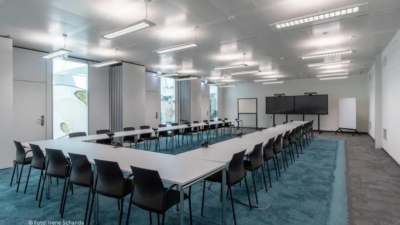 Großer Konferenzraum mit U-förmiger Tischordnung, modernem Teppichboden und integrierten Bildschirmen für Präsentationen.