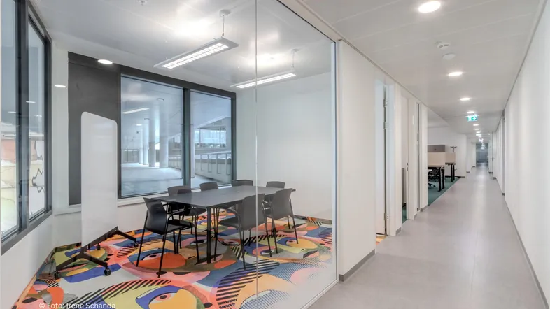 Modernes Besprechungszimmer mit Glastrennwand, farbenfrohem Teppich und Blick auf die Umgebung.