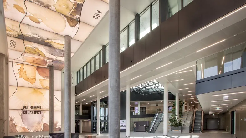 Großzügige, moderne Lobby mit hohen Decken, künstlerischer Deckenverkleidung und viel Tageslicht.