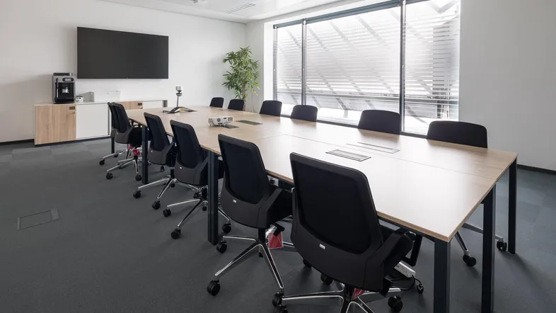 Moderner Konferenzraum mit großem Tisch, bequemen Stühlen und integriertem Bildschirm für Präsentationen.