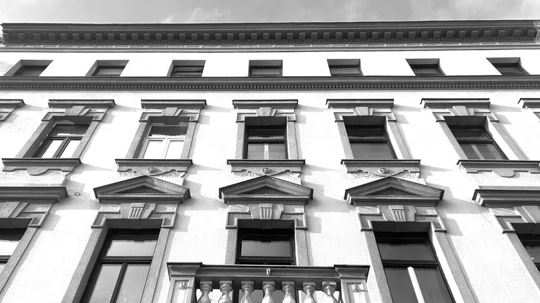 Historische Fassade eines Altbaus mit reich verzierten Fenstern und einem kleinen Balkon.