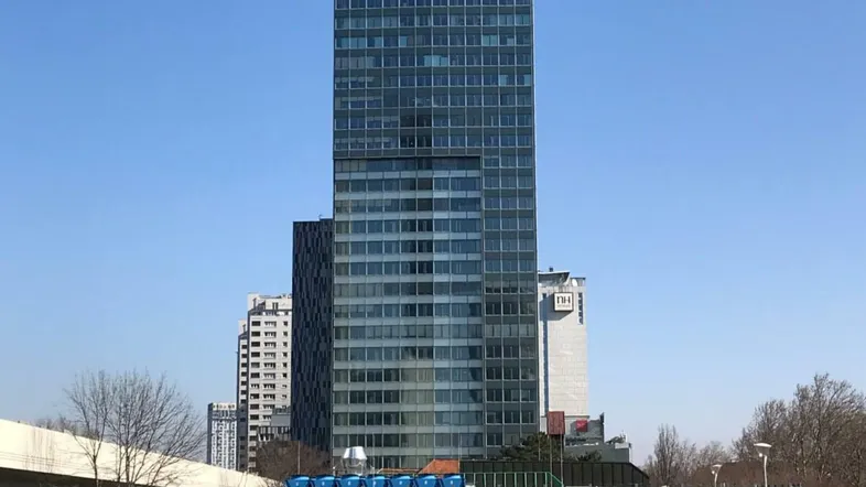 Ein modernes Hochhaus mit Glasfassade und klarem Himmel, umgeben von städtischer Infrastruktur und Bäumen.