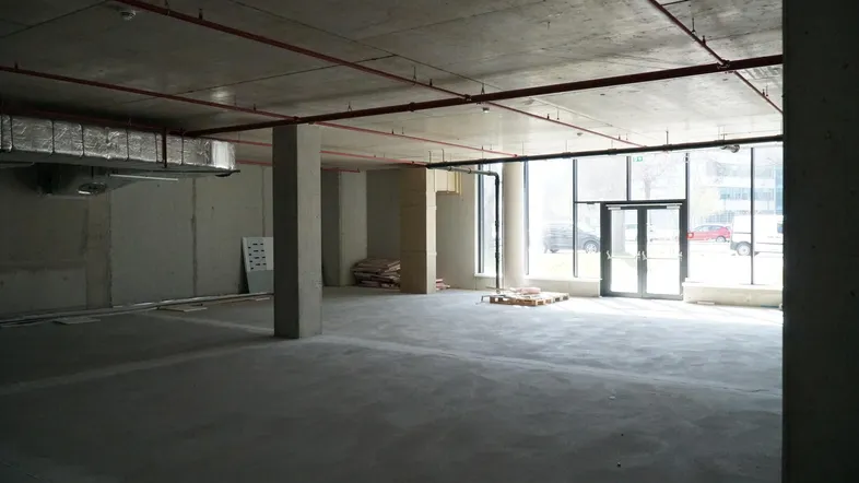 Großer, unfertiger Innenraum mit Betonwänden und -boden, hohen Decken und großen Fenstern, bereit für den Ausbau.